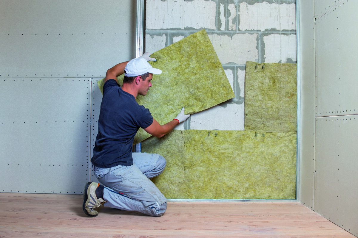 Worker insulating a room wall with mineral rock wool thermal ins